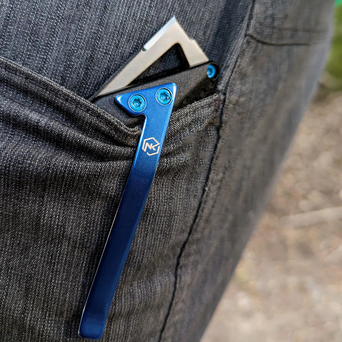 Knife with glass breaker on end of black handle, clipped with blue clip in a pocket with a blurred natural background.