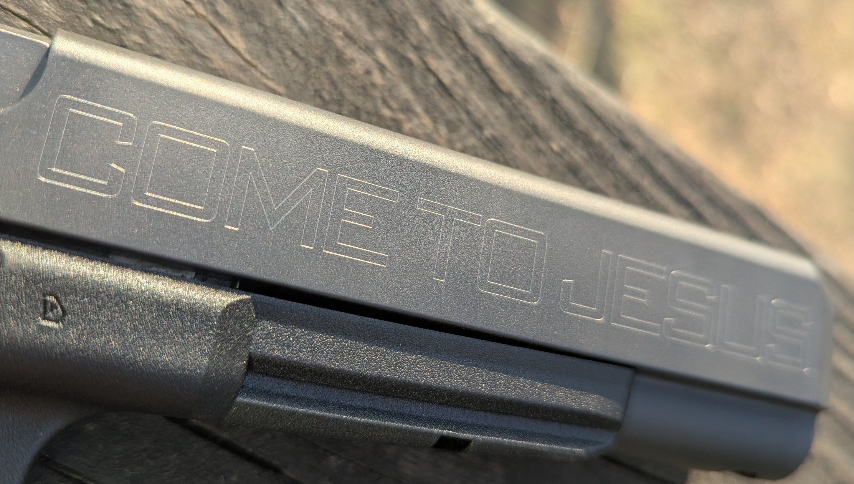 Close-up of a gun with 'COME TO JESUS' engraved on it, blurred background