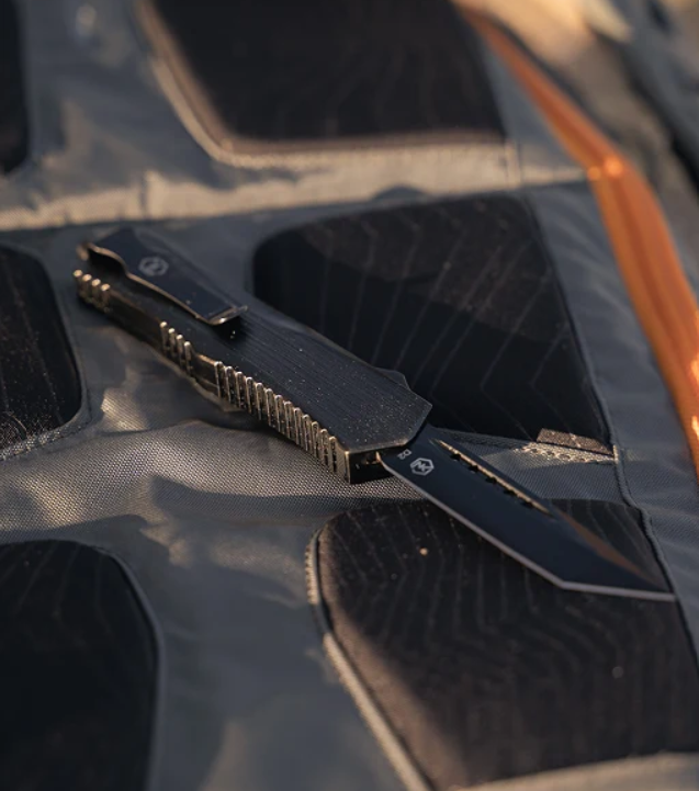 Black OTF knife with black wood grain patterned handle, black belt clip, and black blade on grey and black textured surface.