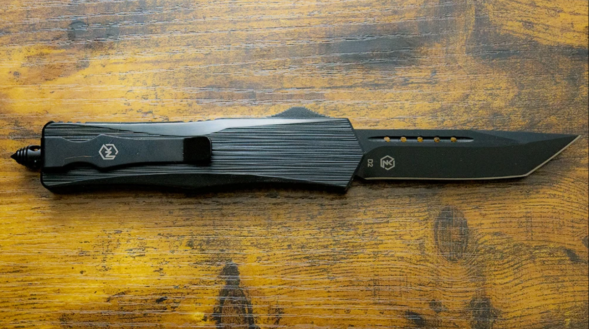 A black folding pocket knife with a textured handle and partially serrated blade, resting on a rustic wooden surface.