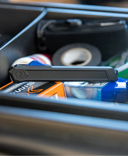 Black pocket knife featuring blue deployment switch and glass break on top of a can in a car's storage compartment