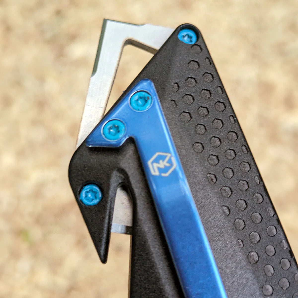 Close-up of a glass breaker that also functions as a box cutter, shown with textured black handle with blue belt clip and screws on a blurred natural background.